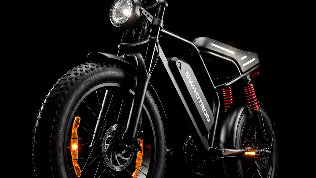 Low front three-quarter view of the SWAGTRON UrbanCruise e-bike, showing its knobby 20-inch by 4-inch front fat tire, caged round headlight and red rear coil-over shocks on a black background