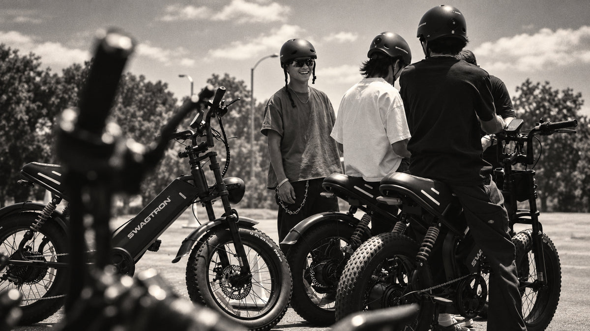 Black-and-white photo of helmeted riders talking beside a row of SWAGTRON e-bikes in a parking lot
