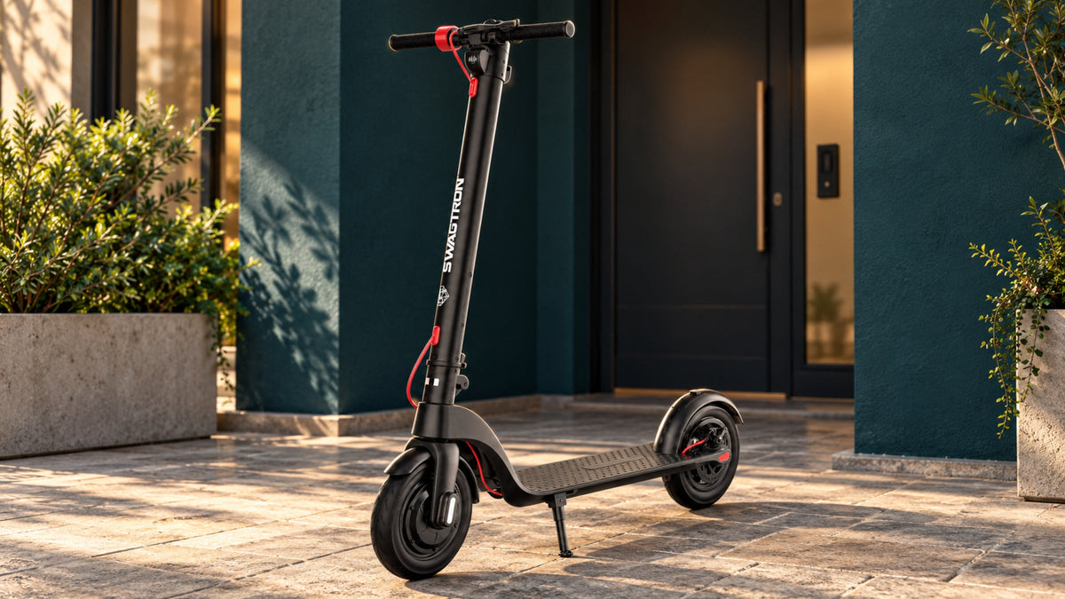 SWAGTRON electric kick scooter parked on a stone patio outside a teal-painted building entrance in warm sunlight