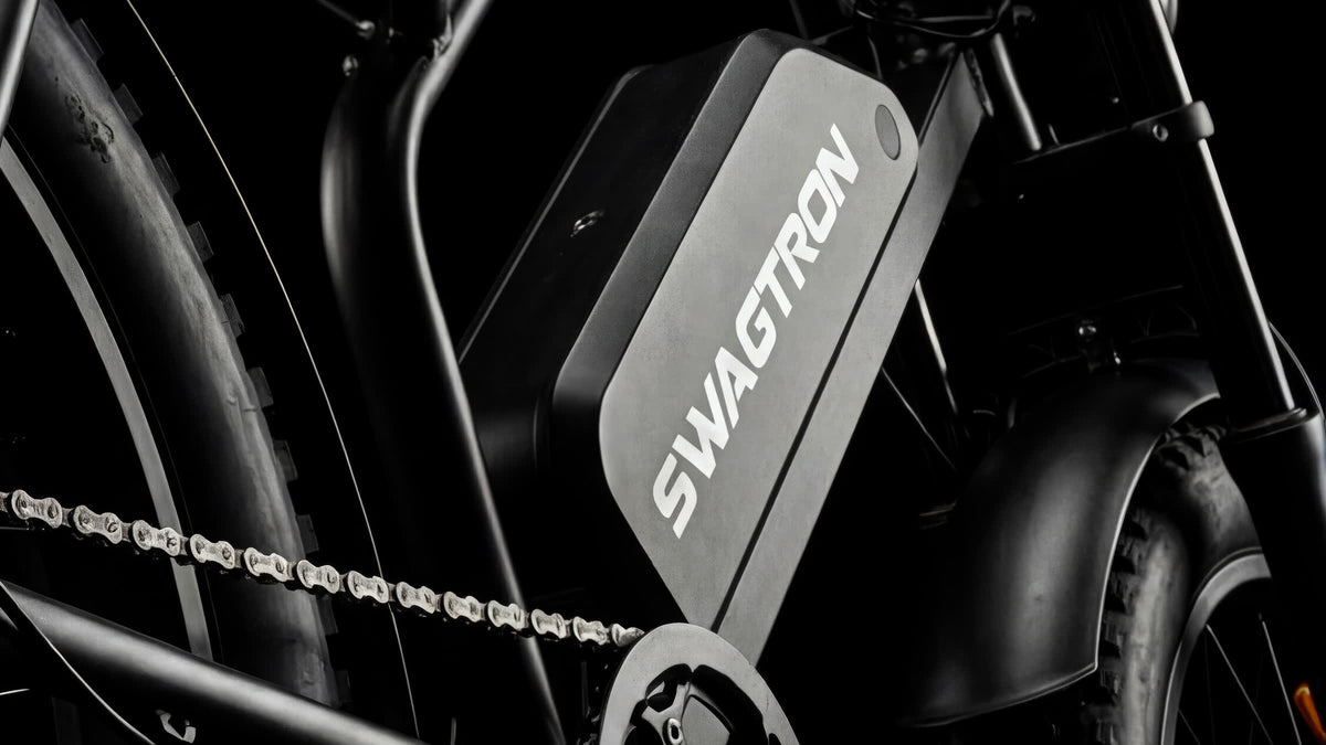 Close-up of the battery pack on a SWAGTRON UrbanCruise e-bike, with the SWAGTRON wordmark, chain and frame on black