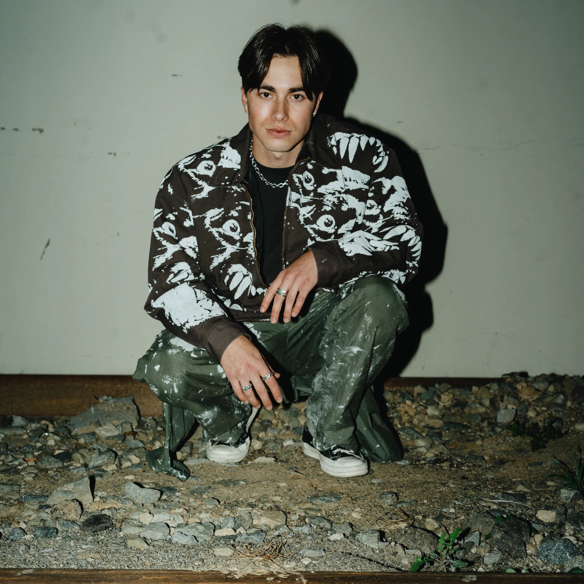 Austin Mollno crouching against a pale wall in a printed jacket.