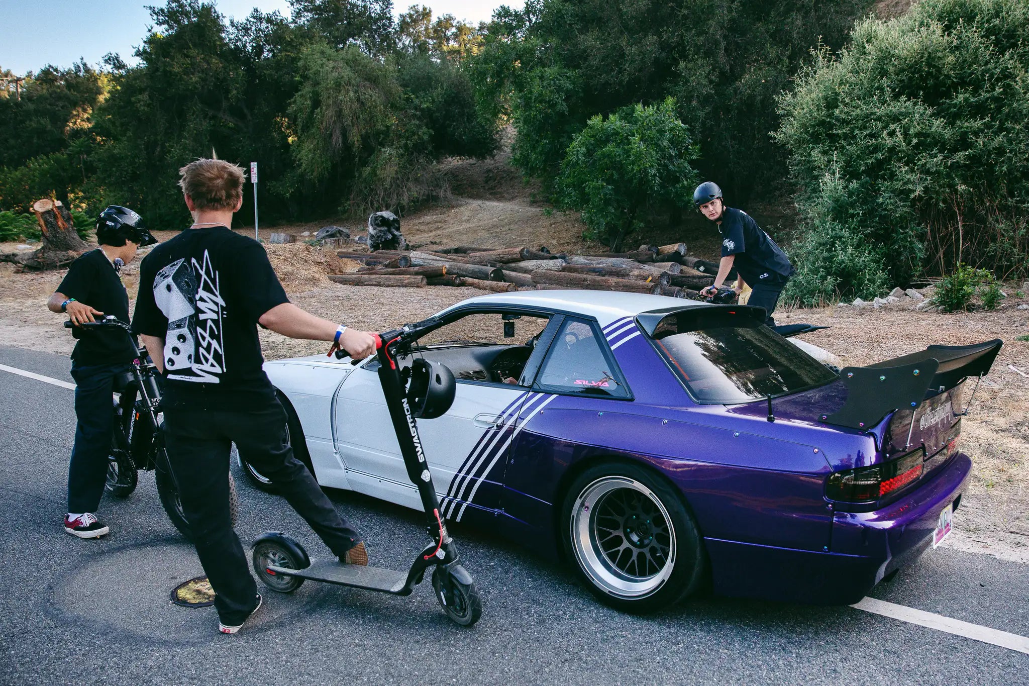 A rider walks a SWAGTRON scooter past the purple-and-white Nissan S13 drift car.