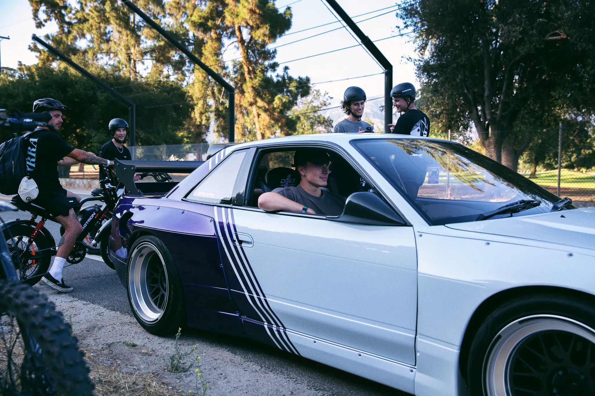 Riders gather around the white-and-purple Nissan S13 drift car, UrbanCruise e-bikes alongside.